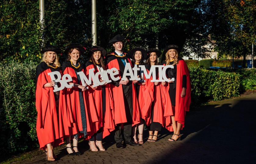 Doctoral students at the MIC Conferring Ceremonies holding an MIC sign