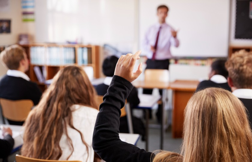 Student raising arm in front of teacher at top of the class 