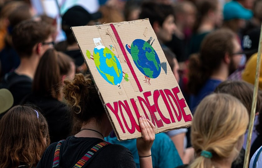 Climate change rally with protestor holding homemade sign with 'You decide' and various images of the world on it