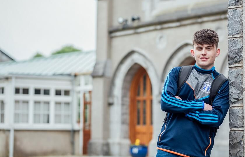 male undergraduate student in MIC branded sports top leaning against wall in the Quad in MIC Limerick