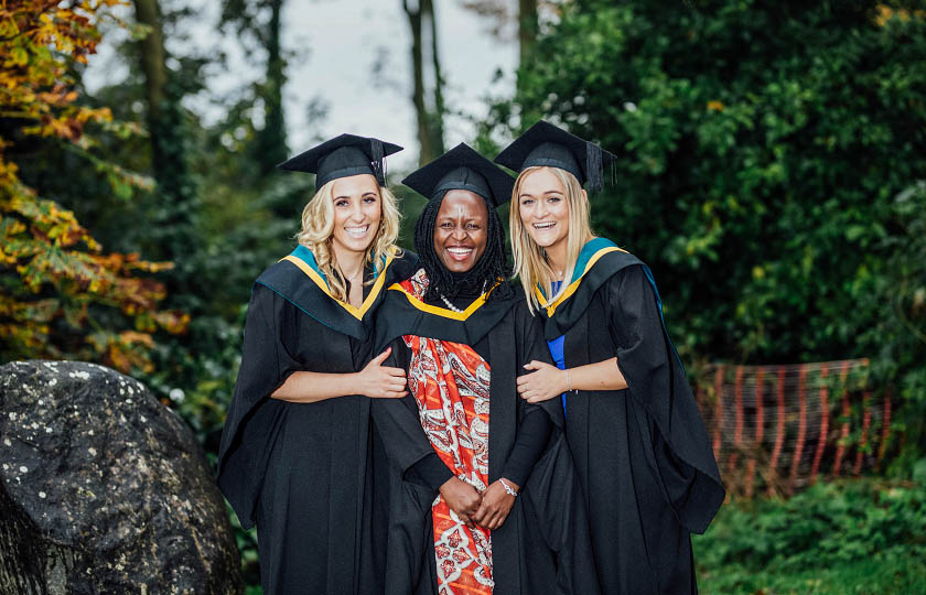 Three female graduates standing close and smiling.