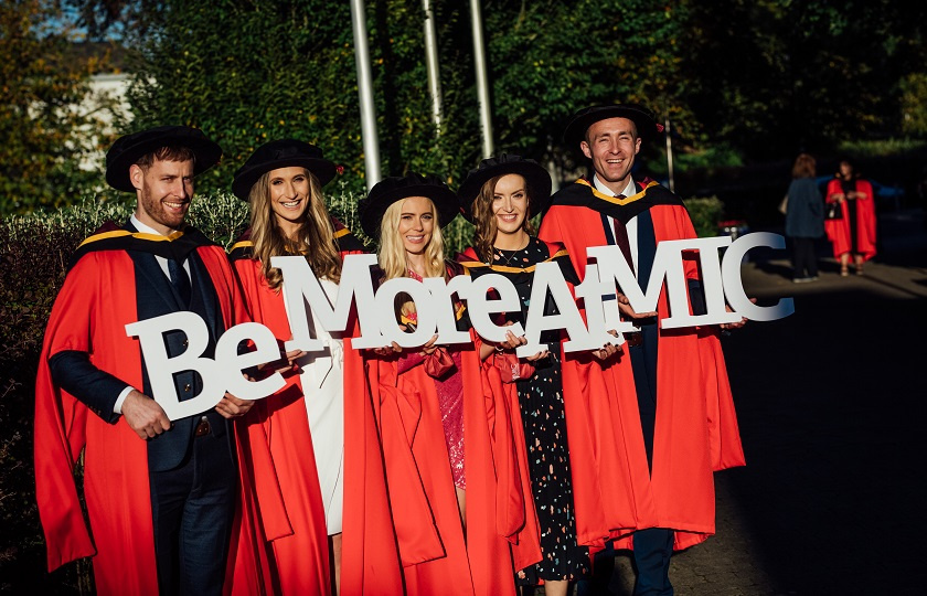 Graduates holding a sign 'Be More At MIC' at Mary Immaculate College Graduation.