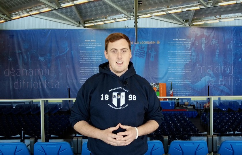 Man standing looking at the camera in the graduation hall wearing an MIC branded hoody