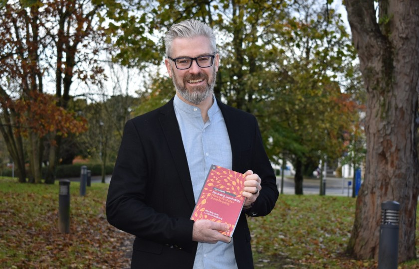 Dr John Morrissey holding a copy of his book