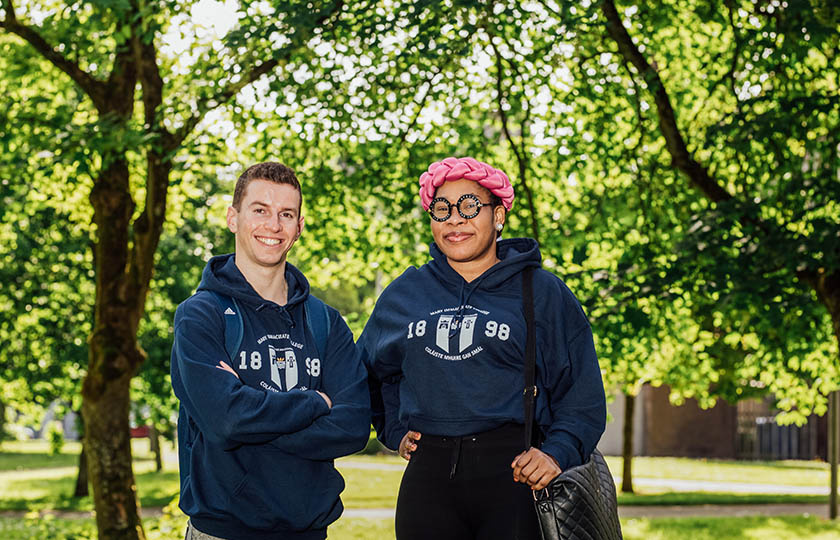 Male and female undergraduates wearing MIC branded hoodies, standing among trees on MIC college grounds.