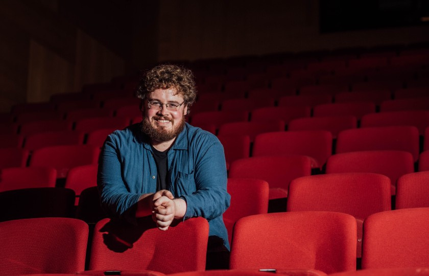 Liam pictured sitting in red theatre seats with dark atmospheric background