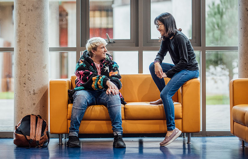 Two students sitting on a yellow couch in reception at MIC Limerick.