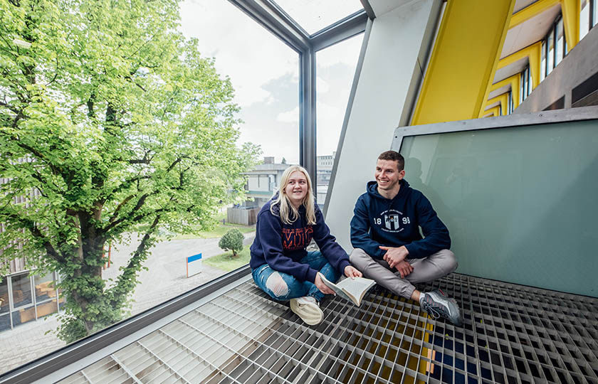 Male and female student sitting inside a large window on MIC Limerick campus.
