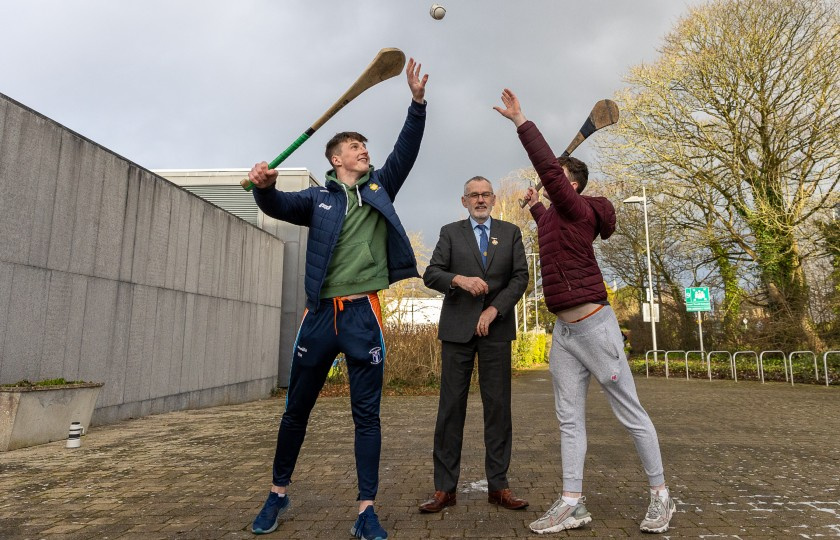 Uachtarán CLG Larry McCarthy with MIC hurlers Diarmuid Ryan and Michael O'Flynn to his right and left holding hurleys and reaching for sliotar.