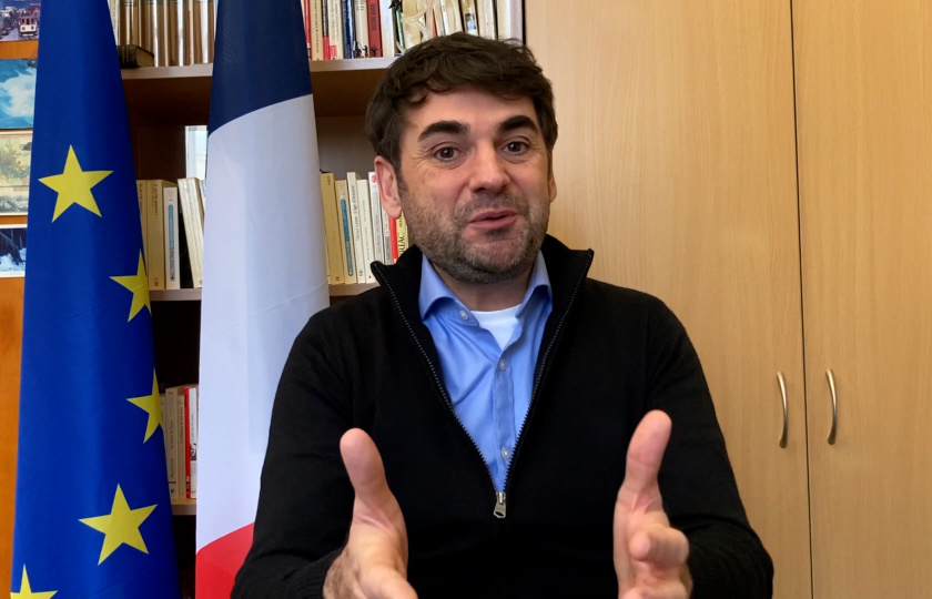 Dr Loic Guyon sitting in front of a French and European flag