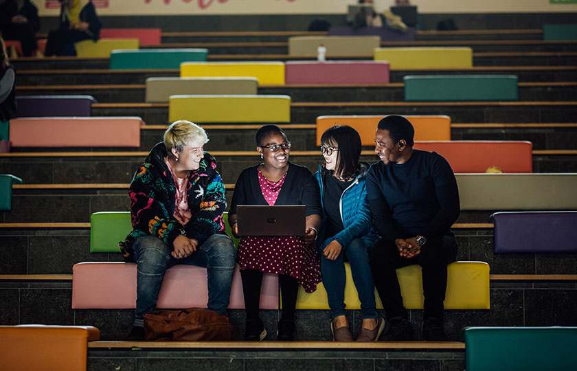 Four postgraduate students sitting on the steps in the Tara building looking at a laptop.
