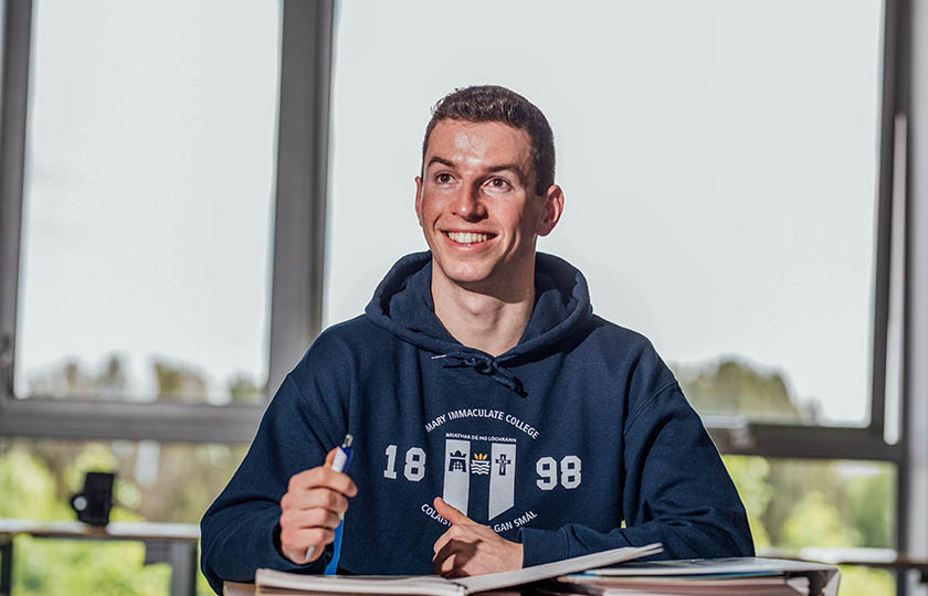 Undergraduate student wearing MIC branded hoodie with a book open in front of him.