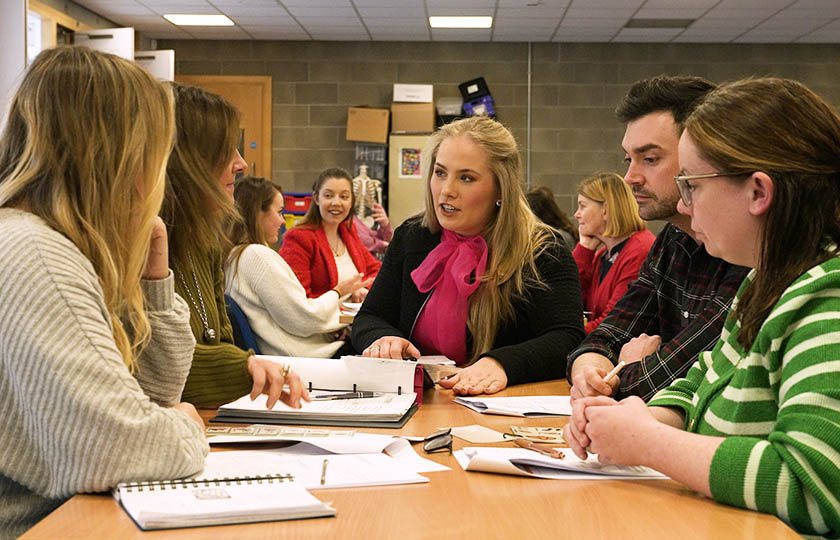 Graphic for Graduate Certificate/Diploma in Autism Studies - lecturer and students sitting around a table with books and notes open on the table..