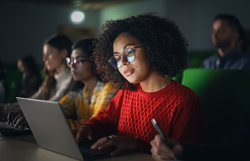 Woman sitting in class with other students looking at her laptop screen.