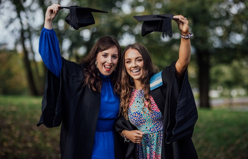 Two female graduates holding their graduation caps above their heads