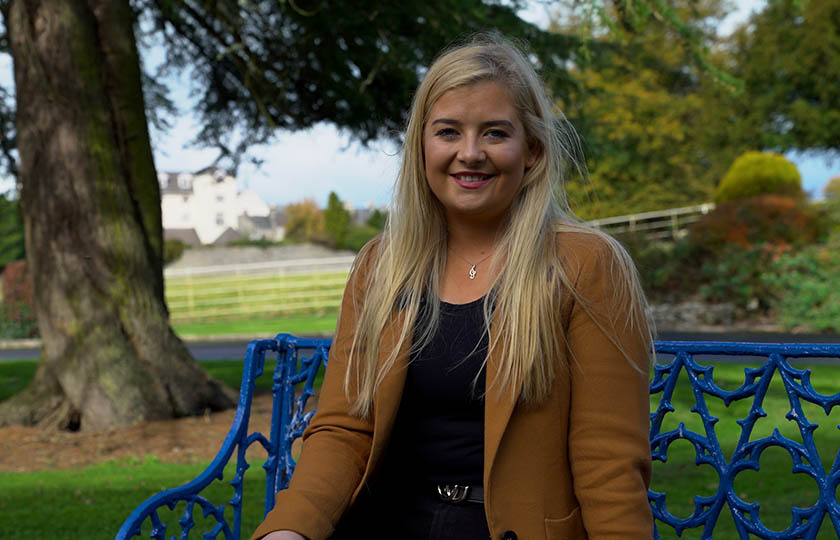 Female student pictured sitting on a blue bench