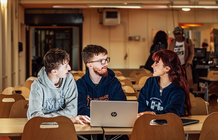 Three students sitting at an open laptop.
