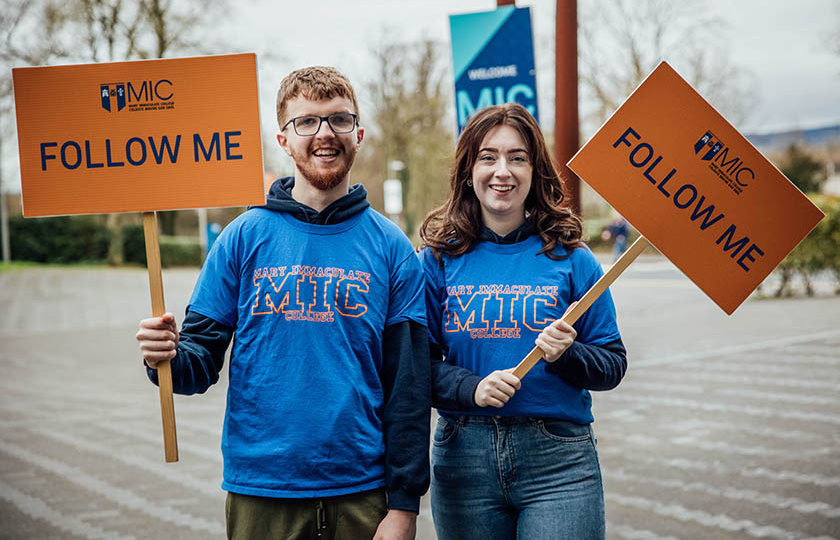 Two MIC students holding signs saying Follow me.