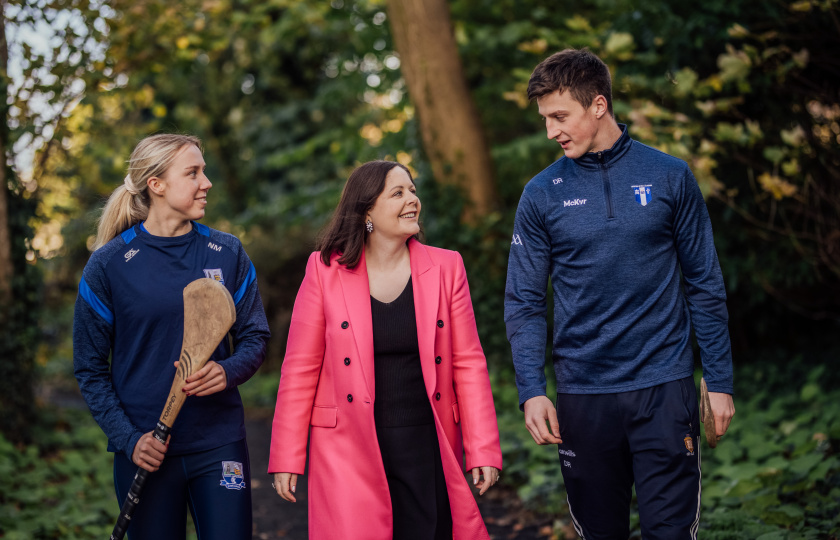Professor Niamh Hourigan pictured with Niamh Murphy and Diarmuid Ryan walking in a wooded area. Diarmuid and Niamh are carrying hurleys.