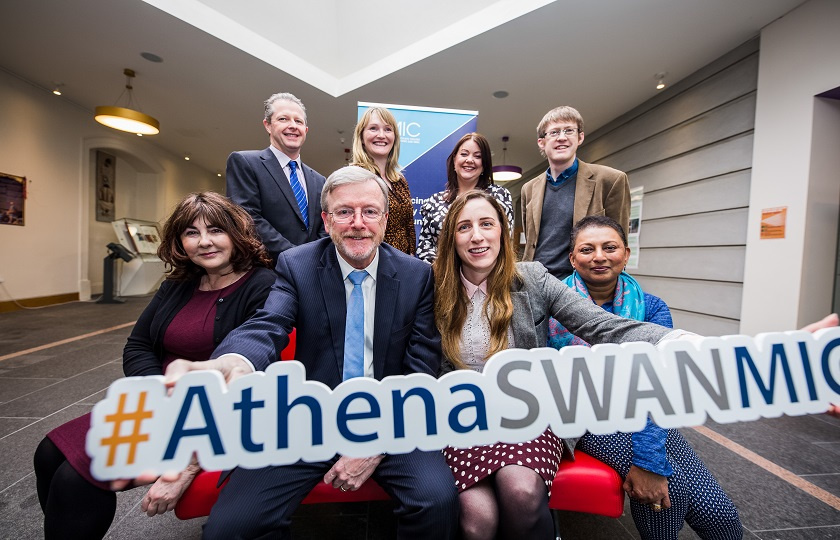 A group of MIC staff holding an Athena Swan sign in the foyer of the Foundation Building.