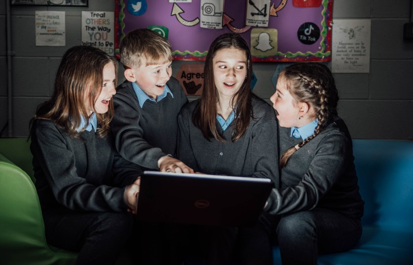 Three female and one male student looking excited and surprised at laptop screen