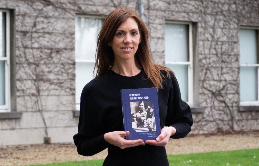 Sarah O'Brien holding her book in front of College building