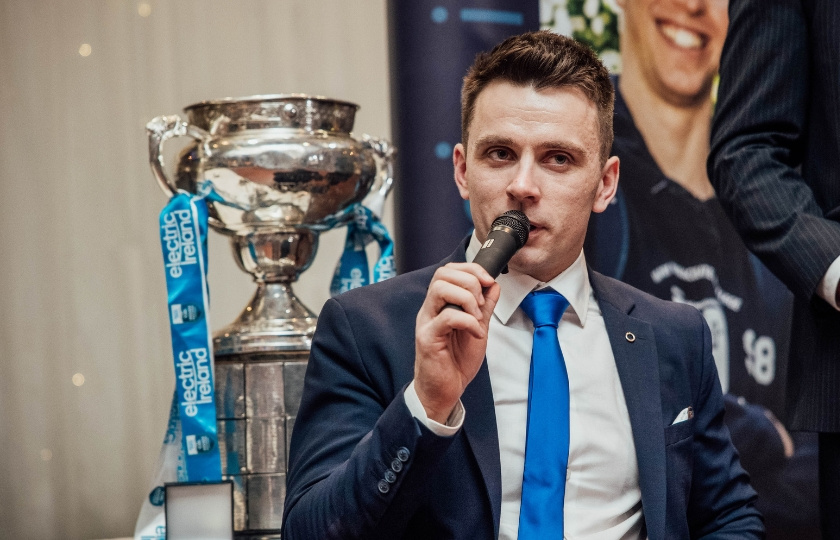 Jamie Wall speaks into a microphone. The Fitzgibbon Cup is pictured behind him