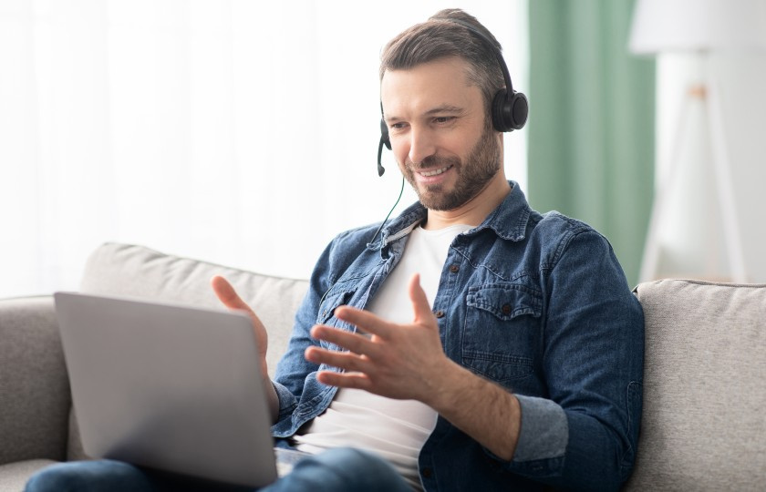 Male sitting on couch wearing headphones and looking at a laptop on his lap