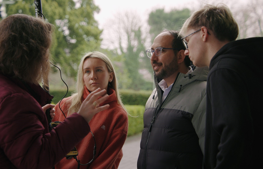 Group of three people standing outside listening attentively to another person talking to them