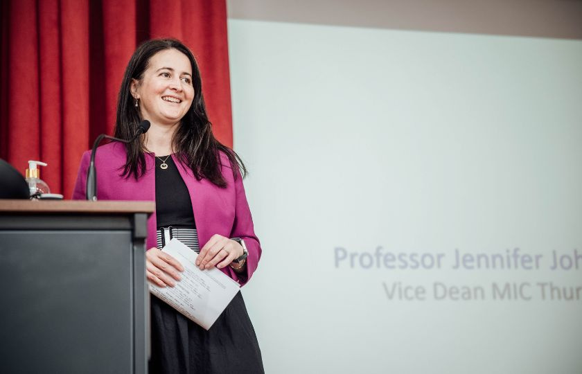A smiling woman standing at a podium and speaking into a microphone.
