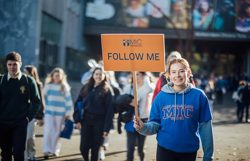 Student holding a Follow me sign on open days at MIC