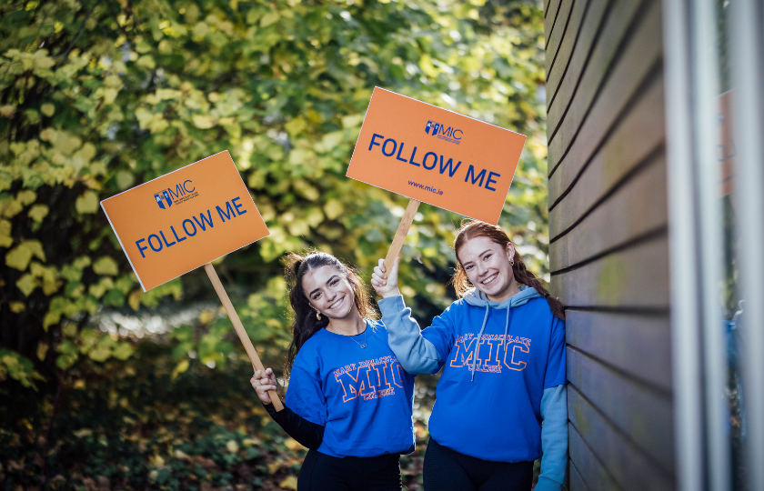 Two female students holding tour guide signs for a college open days