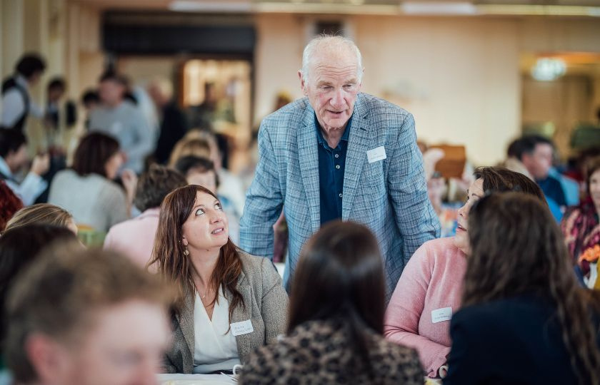 A man standing by a table of former students talking to them