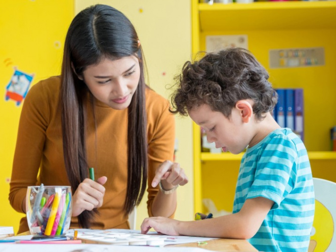 Stock image of a young woman helping a small boy to draw