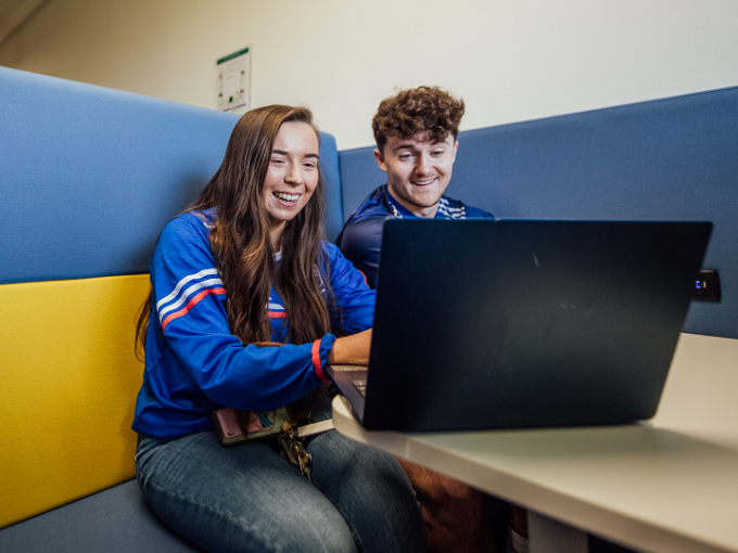 A female and and male student are sitting at a table and looking into a laptop screen