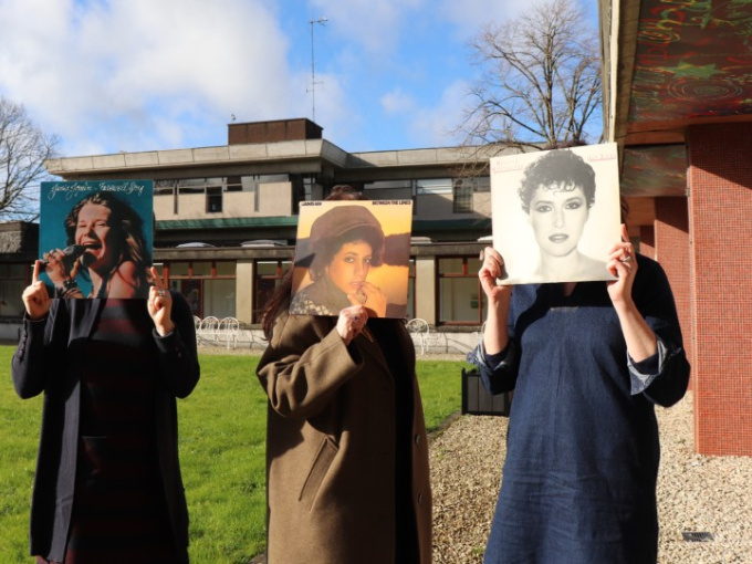 FemFest committee members holding vinyl records in front of their faces, standing in the quad at MIC
