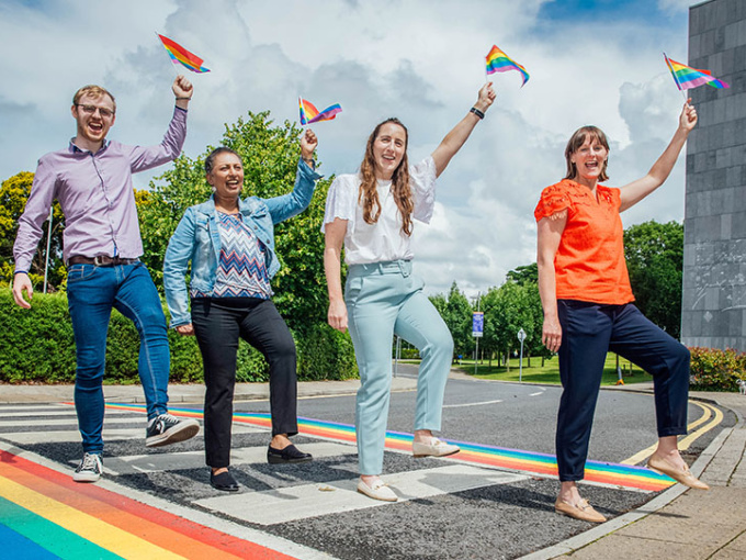 MIC staff and MISU president walking across the pride pedestrian crossing at MIC holding up pride flags.